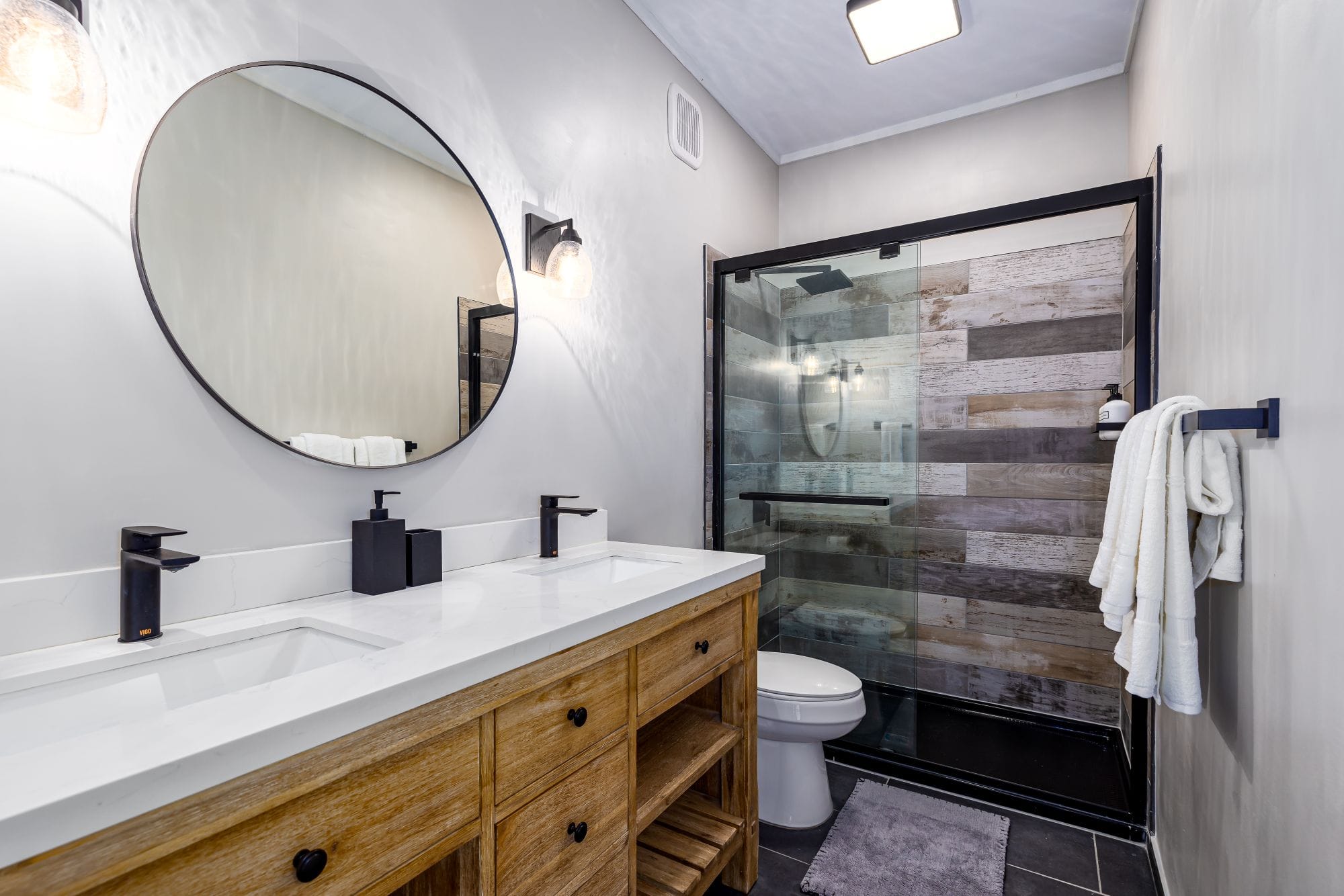 Double vanity with a round mirror and a wood-tiled walk-in shower