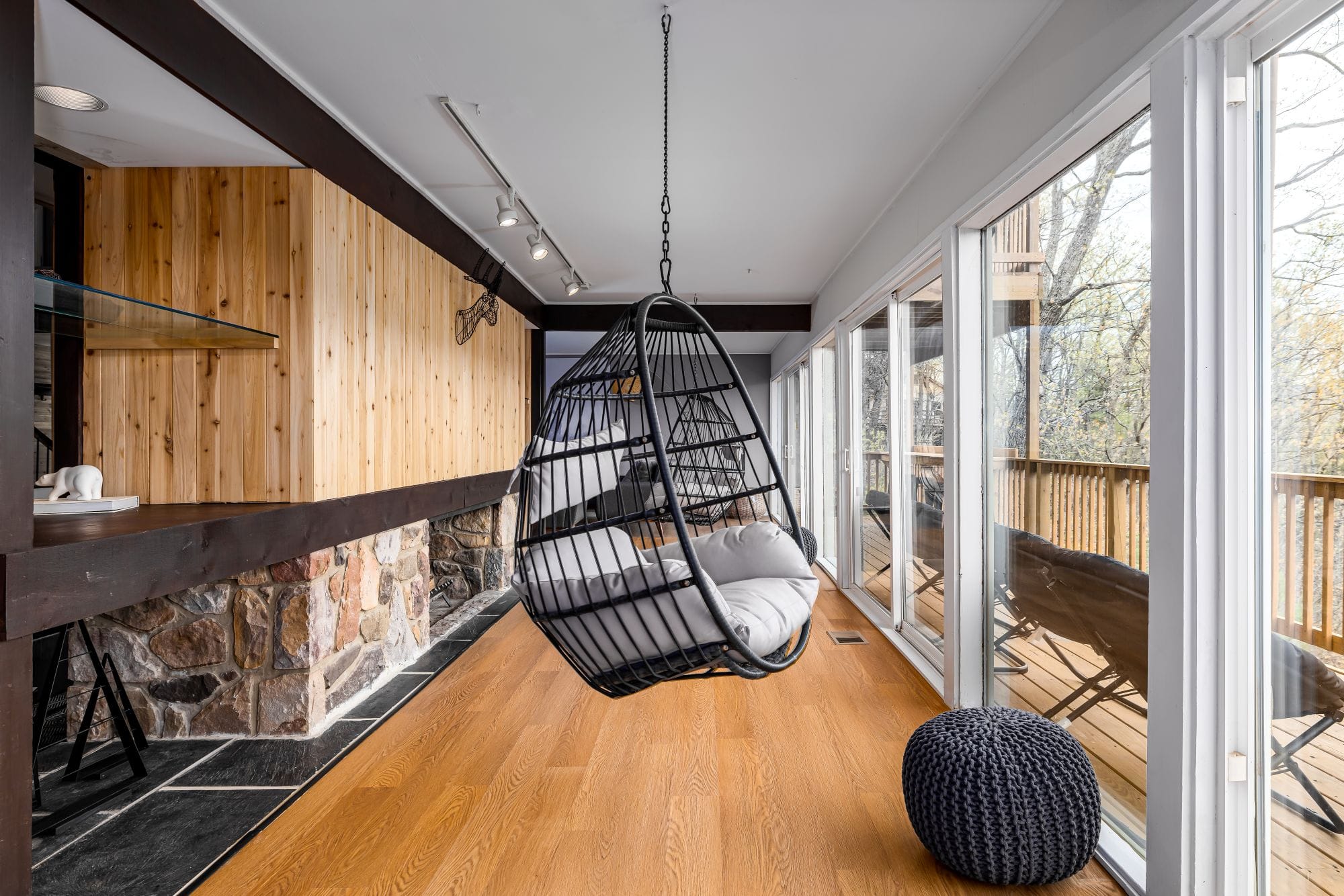Sunroom nook with a hanging egg chair, cedar walls, and sliding doors to the deck