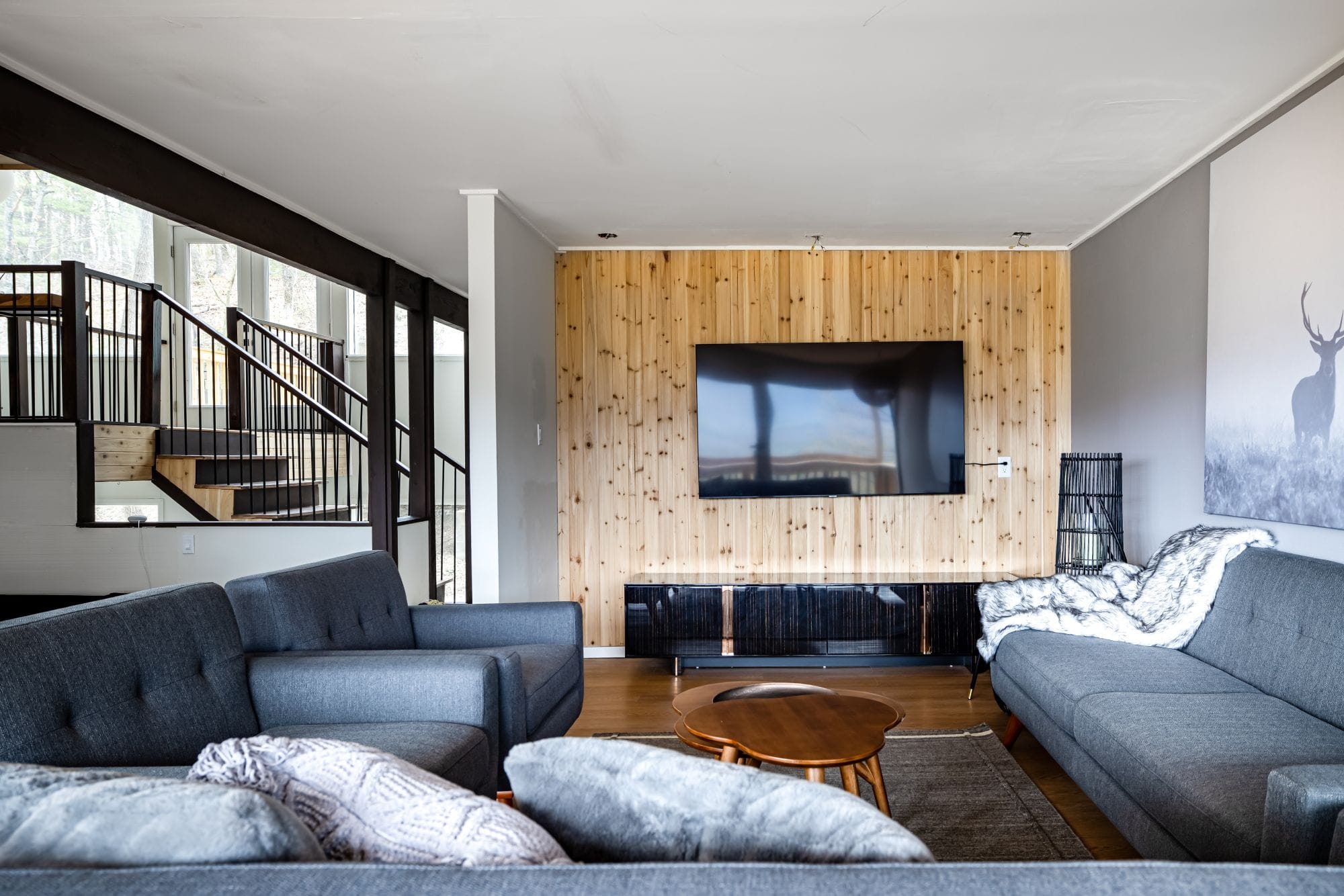 Living room with a mounted TV on a cedar-panel wall beside the staircase