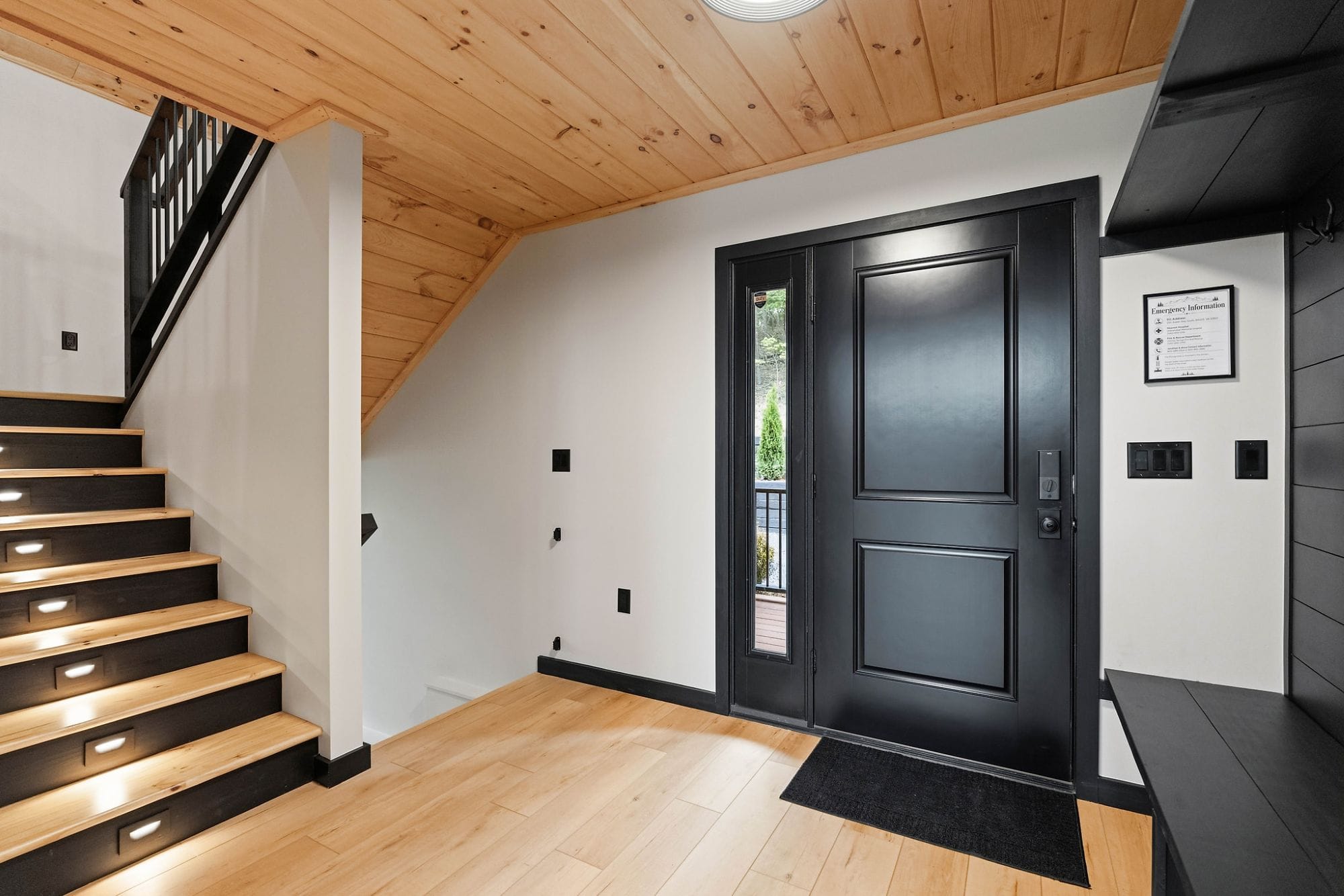 Entry foyer with warm wood, a black steel staircase with lit treads, and a black front door