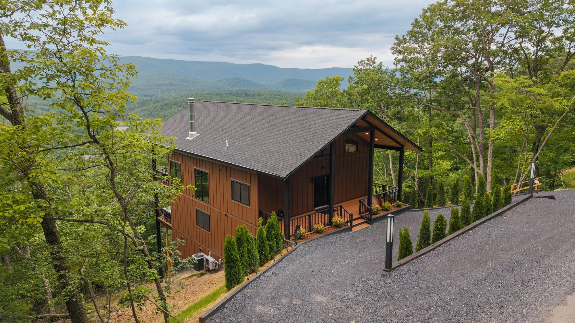 The Cabin's cedar-and-black facade glowing under a covered porch at dusk, with an EV charger in the drive