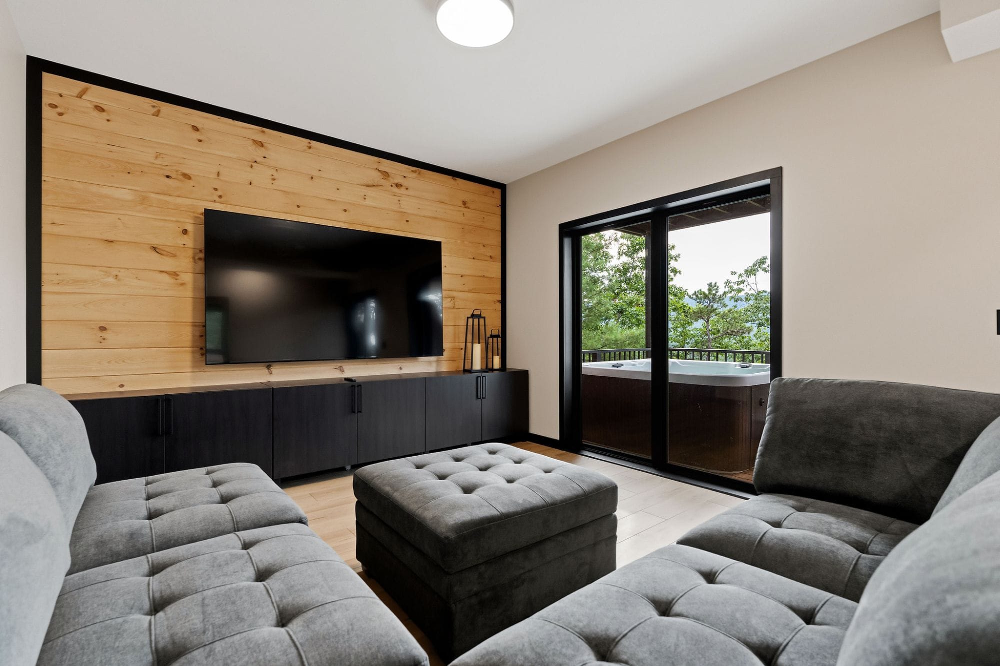 Lower-level TV lounge with a tufted sectional and sliding doors to the hot tub