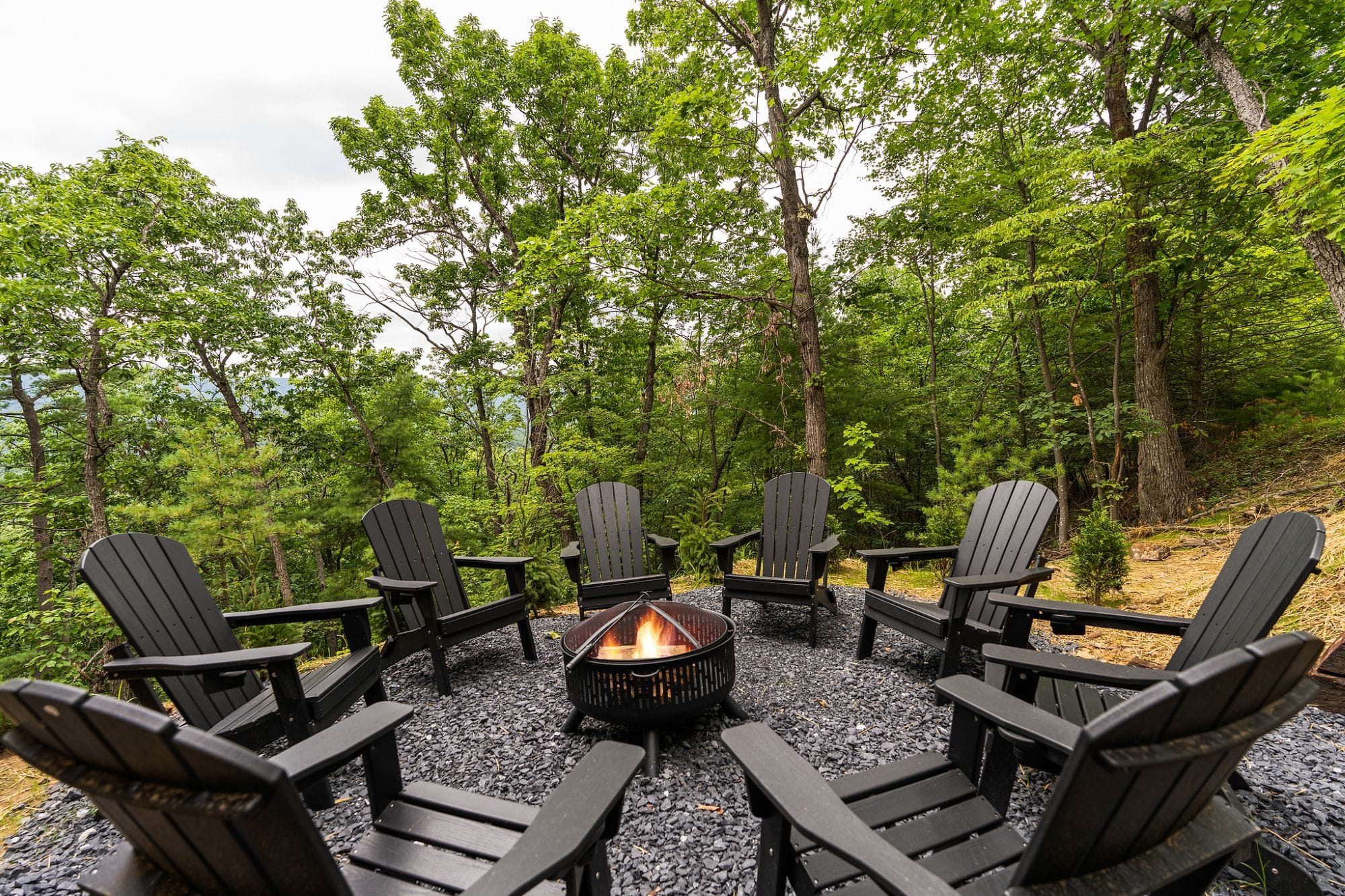 Fire pit ringed with black Adirondack chairs among the trees